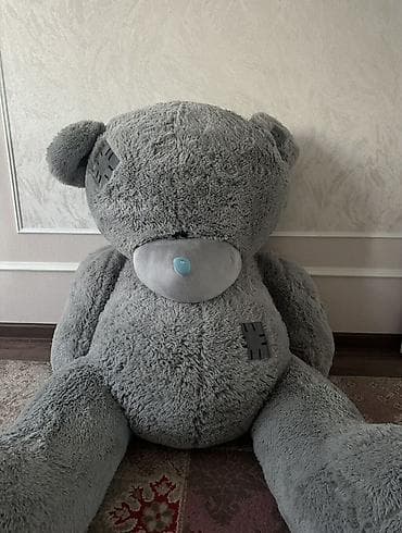 Большой плюшевый мишка серого цвета с заплатками. Этот медведь станет