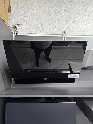 Современная кухонная вытяжка из черного стекла. Имеет наклонный