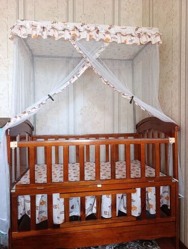 Деревянная детская кроватка, оснащенная балдахином и москитной сеткой