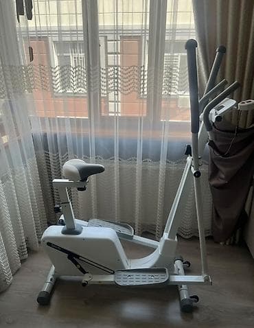 Белый велоэргометр с серым сиденьем и ручками. Оснащен регулируемыми