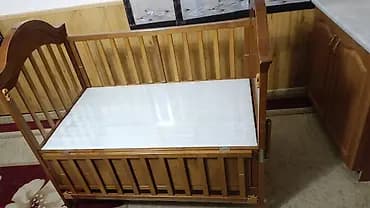 Деревянная детская кроватка светлого оттенка, оснащенная колесиками